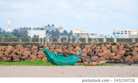 A traditional fishing boat rests on a sandy tropical shoreline against a rocky seawall 143250728