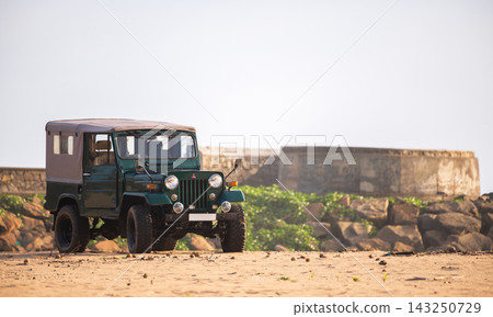 Vintage-style four-wheel-drive jeep parked on a sandy beach Vintage-style four-wheel-drive jeep parked on a sandy beach 143250729