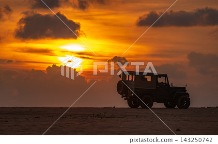 Vintage Off-Road Jeep on the beach, silhouette against a dramatic sunset backdrop Vintage Off-Road Jeep on the beach, silhouette against a dramatic sunset backdrop 143250742