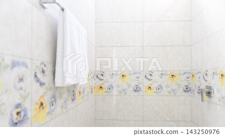 A clean white towel hangs on a towel rack in a tiled bathroom wall A clean white towel hangs on a towel rack in a tiled bathroom wall 143250976