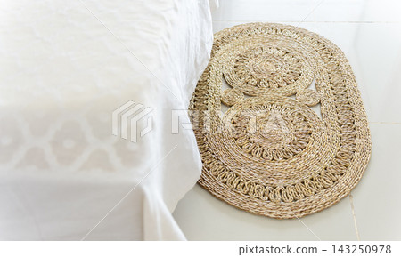 Woven rattan floor mat beside white bed 143250978