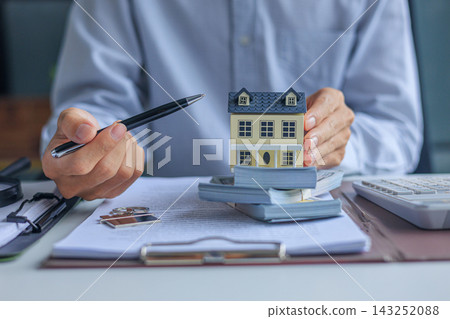 Real estate broker desk with house model, money, and calculator. Mortgage estimation and property purchasing concept. Real estate broker desk with house model, money, and calculator. Mortgage estimation and property purchasing concept. 143252088