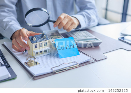 Businessman using magnifying glass looking over contract document, miniature house and loan money budget for real estate financial analyzing and investigating Businessman using magnifying glass looking over contract document, miniature house and loan money budget for real estate financial analyzing and investigating 143252325