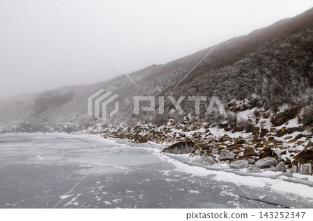 完全冰封的冬季湖岸和白雪皚皚的山坡 完全冰封的冬季湖岸和白雪皚皚的山坡 143252347