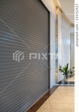 Closed Retail Store With Metal Rolling Shutter Inside Modern Shopping Mall Corridor With Potted Plant Closed Retail Store With Metal Rolling Shutter Inside Modern Shopping Mall Corridor With Potted Plant 143252417