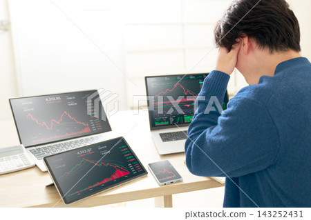 一名年輕男子雙手抱頭,看著多個裝置上顯示的下跌趨勢圖表。 一名年輕男子雙手抱頭,看著多個裝置上顯示的下跌趨勢圖表。 143252431