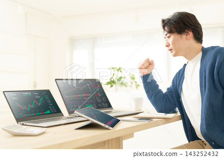 一名二十多歲的男子在家看股票圖表時，做出了一個得意的手勢。 143252432