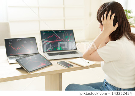 一位年輕女子雙手抱頭,看著多個裝置上顯示的下降趨勢圖。 一位年輕女子雙手抱頭,看著多個裝置上顯示的下降趨勢圖。 143252434