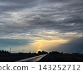 Wet asphalt road leading through a rural landscape under a dramatic cloudy sky with a vibrant rainbow appearing as a beacon of hope after a heavy rain shower 143252712