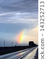 Wet road reflecting a vibrant rainbow arcing across a dramatic cloudy sky during sunset in a rural landscape with power lines, highlighting hope after a rainstorm 143252713