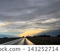Wet asphalt road reflecting a vibrant rainbow stretching across a cloudy sky as the sun sets over a tranquil rural landscape with power lines, illustrating hope and natural beauty after a rainstorm.Hi 143252714