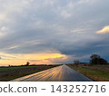 A stormy sunset illuminates a rural landscape with dramatic dark clouds over a vast open field. 143252716