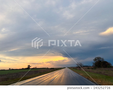 A stormy sunset illuminates a rural landscape with dramatic dark clouds over a vast open field. A stormy sunset illuminates a rural landscape with dramatic dark clouds over a vast open field. 143252716
