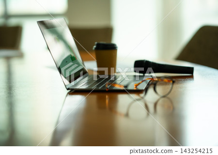 A laptop, coffee cup, and microphone are placed on the conference room table. 143254215