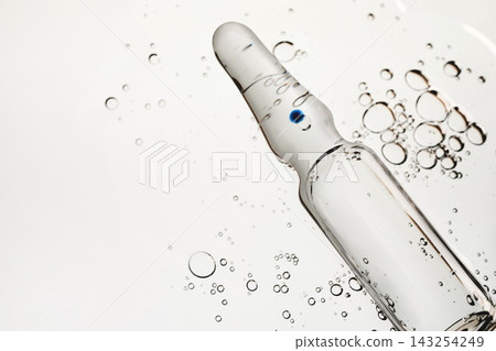 Clear glass ampoule containing liquid and blue dot, surrounded by various size bubbles Clear glass ampoule containing liquid and blue dot, surrounded by various size bubbles 143254249