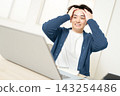 A young man sits in front of his computer, holding his head in frustration. 143254486