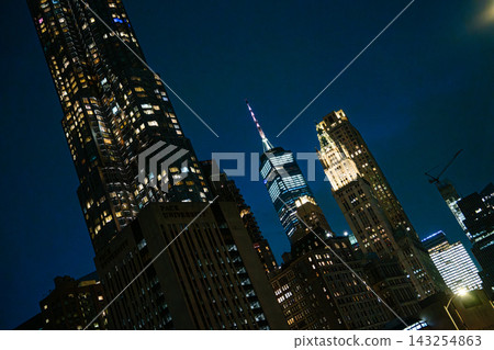 Illuminated skyscrapers of Lower Manhattan rise into the night sky with One World Trade Center glowing above the city skyline. Bright windows and modern towers highlight the vibrant architecture of Illuminated skyscrapers of Lower Manhattan rise into the night sky with One World Trade Center glowing above the city skyline. Bright windows and modern towers highlight the vibrant architecture of 143254863