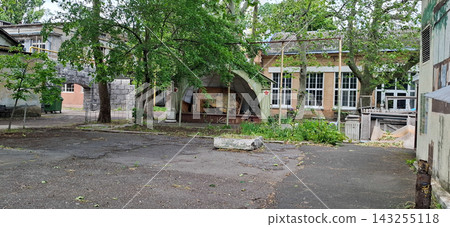 Odessa Film Studio. Old abandoned industrial courtyard with weathered buildings cracked asphalt surface and green trees on background. Odessa Film Studio. Old abandoned industrial courtyard with weathered buildings cracked asphalt surface and green trees on background. 143255118