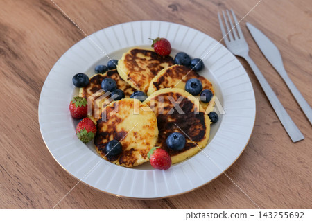Pancakes with blueberries on a white plate beside silver cutlery on a wooden table. Minimal breakfast styling creates a clean food photography concept Pancakes with blueberries on a white plate beside silver cutlery on a wooden table. Minimal breakfast styling creates a clean food photography concept 143255692