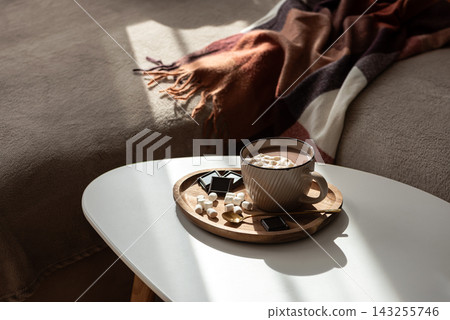 Cozy hot chocolate with marshmallows and chocolate on a tray next to a warm blanket. Cozy hot chocolate with marshmallows and chocolate on a tray next to a warm blanket. 143255746
