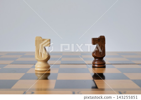 Light and dark chess knights face each other on a glossy wooden board. The minimal duel represents competition, confrontation, and strategic opposition Light and dark chess knights face each other on a glossy wooden board. The minimal duel represents competition, confrontation, and strategic opposition 143255851