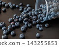 An overturned clear plastic cup spills blueberries across a dark surface. Fruit motion and abundance illustrate harvest, snack preparation, and food spill concepts. 143255853