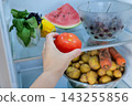 Human hand reaching for fresh red tomato inside open refrigerator 143255856