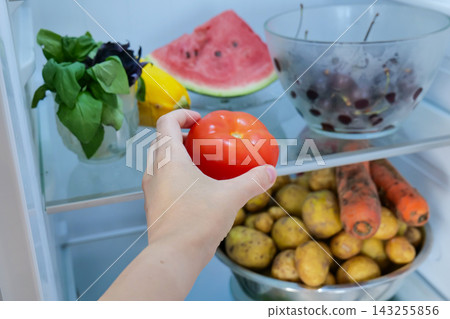 Human hand reaching for fresh red tomato inside open refrigerator Human hand reaching for fresh red tomato inside open refrigerator 143255856
