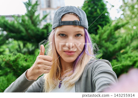 Teenage girl taking selfie showing thumbs up gesture outdoors close up 143255914