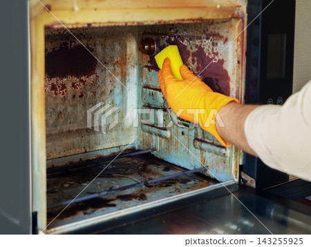 man performs kitchen oven cleaning to clear rust, grime, and grease. He uses a cleaning sponge and protective gloves on a dirty appliance for routine daily home household chores. man performs kitchen oven cleaning to clear rust, grime, and grease. He uses a cleaning sponge and protective gloves on a dirty appliance for routine daily home household chores. 143255925