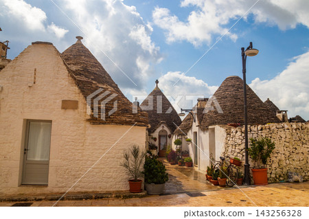 Scenic view of a picturesque narrow street with traditional historic white trulli houses in Alberobello, Apulia, Italy Scenic view of a picturesque narrow street with traditional historic white trulli houses in Alberobello, Apulia, Italy 143256328