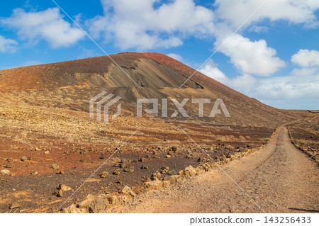 Empty dirt trail past Montana Colorada volcano cone on the route to Calderon Hondo in Fuerteventura, Canary Islands, Spain Empty dirt trail past Montana Colorada volcano cone on the route to Calderon Hondo in Fuerteventura, Canary Islands, Spain 143256433