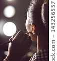 Makeup Artist Applying Finishing Touches To Model Backstage In Dressing Room With Vanity Lights 143256557