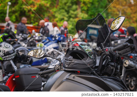 Motorcycle Helmet on Bike, Outdoor motorbike Gathering. Black motorcycle helmet resting on touring bike, outdoor gathering. Rows of parked motorbikes, riders. Biker culture background Motorcycle Helmet on Bike, Outdoor motorbike Gathering. Black motorcycle helmet resting on touring bike, outdoor gathering. Rows of parked motorbikes, riders. Biker culture background 143257021