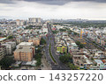 An elevated panoramic view shows dense low-rise neighborhoods and distant apartment towers beneath a broad overcast sky. 143257220