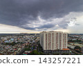 A panoramic elevated view shows dense residential buildings and rooftops beneath a vast sky filled with dark storm clouds. 143257221