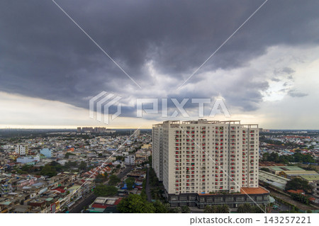 A panoramic elevated view shows dense residential buildings and rooftops beneath a vast sky filled with dark storm clouds. A panoramic elevated view shows dense residential buildings and rooftops beneath a vast sky filled with dark storm clouds. 143257221