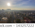 A dense cityscape of rooftops and high-rise buildings stretches toward a hazy horizon beneath diffused sunlight and layered clouds. 143257222