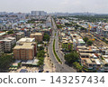 An elevated panoramic view shows dense low-rise neighborhoods, apartment buildings, roads, greenery, and a distant high-rise skyline beneath a hazy sky. 143257434
