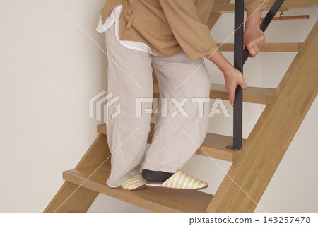 一位老婦人扶著扶手下樓梯。 一位老婦人扶著扶手下樓梯。 143257478