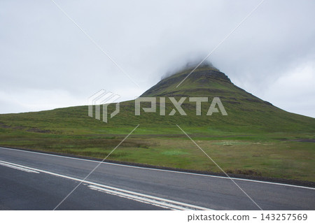 Kirkjufell mountain with peak in clouds and road in Iceland Kirkjufell mountain with peak in clouds and road in Iceland 143257569
