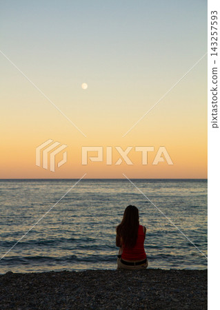 a lonely man sits on the seashore at sunset 143257593
