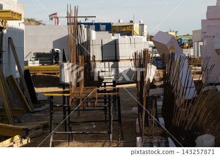 Organizing steel reinforcement bars arranged neatly at a construction site during the assembly phase. Various building materials, scaffolding, and construction equipment are visible in the background Organizing steel reinforcement bars arranged neatly at a construction site during the assembly phase. Various building materials, scaffolding, and construction equipment are visible in the background 143257871