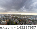 An elevated view shows dense residential buildings, roads, and distant apartment towers beneath a vast overcast sky. 143257957