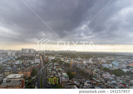 An elevated view shows dense residential buildings, roads, and distant apartment towers beneath a vast overcast sky. An elevated view shows dense residential buildings, roads, and distant apartment towers beneath a vast overcast sky. 143257957
