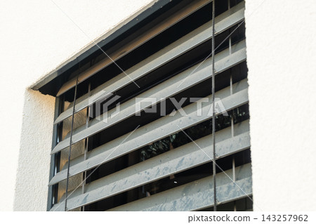 Metal window shutters angled to allow airflow while maintaining security in a residential setting. The surface shows signs of weathering with grime accumulation visible on the slats. Metal window shutters angled to allow airflow while maintaining security in a residential setting. The surface shows signs of weathering with grime accumulation visible on the slats. 143257962