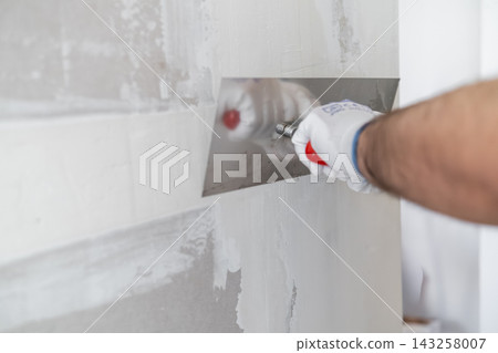 Professional applying a smooth finishing coat to drywall using a stainless steel trowel. Clean and bright working environment with prepared walls visible in the background. Professional applying a smooth finishing coat to drywall using a stainless steel trowel. Clean and bright working environment with prepared walls visible in the background. 143258007