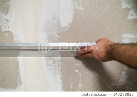 Utilizing a metal straightedge to smooth the joint compound on drywall during a home renovation project. Utilizing a metal straightedge to smooth the joint compound on drywall during a home renovation project. 143258022