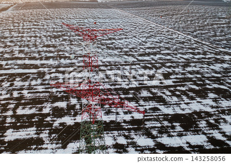 Electricity transmission towers stand tall over vast, snow covered agricultural fields. The contrast between the white snow and the dark soil creates a striking visual effect. Electricity transmission towers stand tall over vast, snow covered agricultural fields. The contrast between the white snow and the dark soil creates a striking visual effect. 143258056