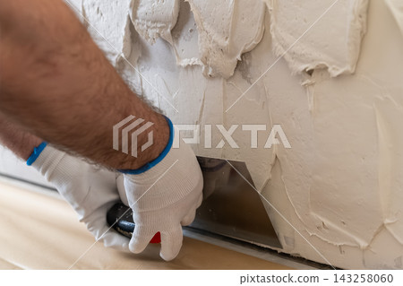 A technician uses a trowel to apply a smooth layer of plaster on the wall surface during an interior renovation. The workspace is clean and well organized, showcasing tools and materials. A technician uses a trowel to apply a smooth layer of plaster on the wall surface during an interior renovation. The workspace is clean and well organized, showcasing tools and materials. 143258060